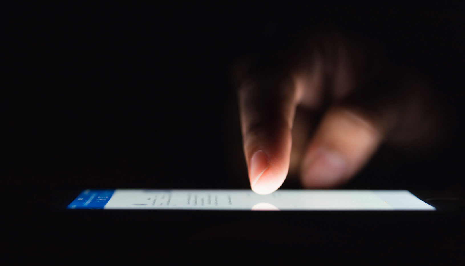 smartphone illuminated in dark with finger touching it