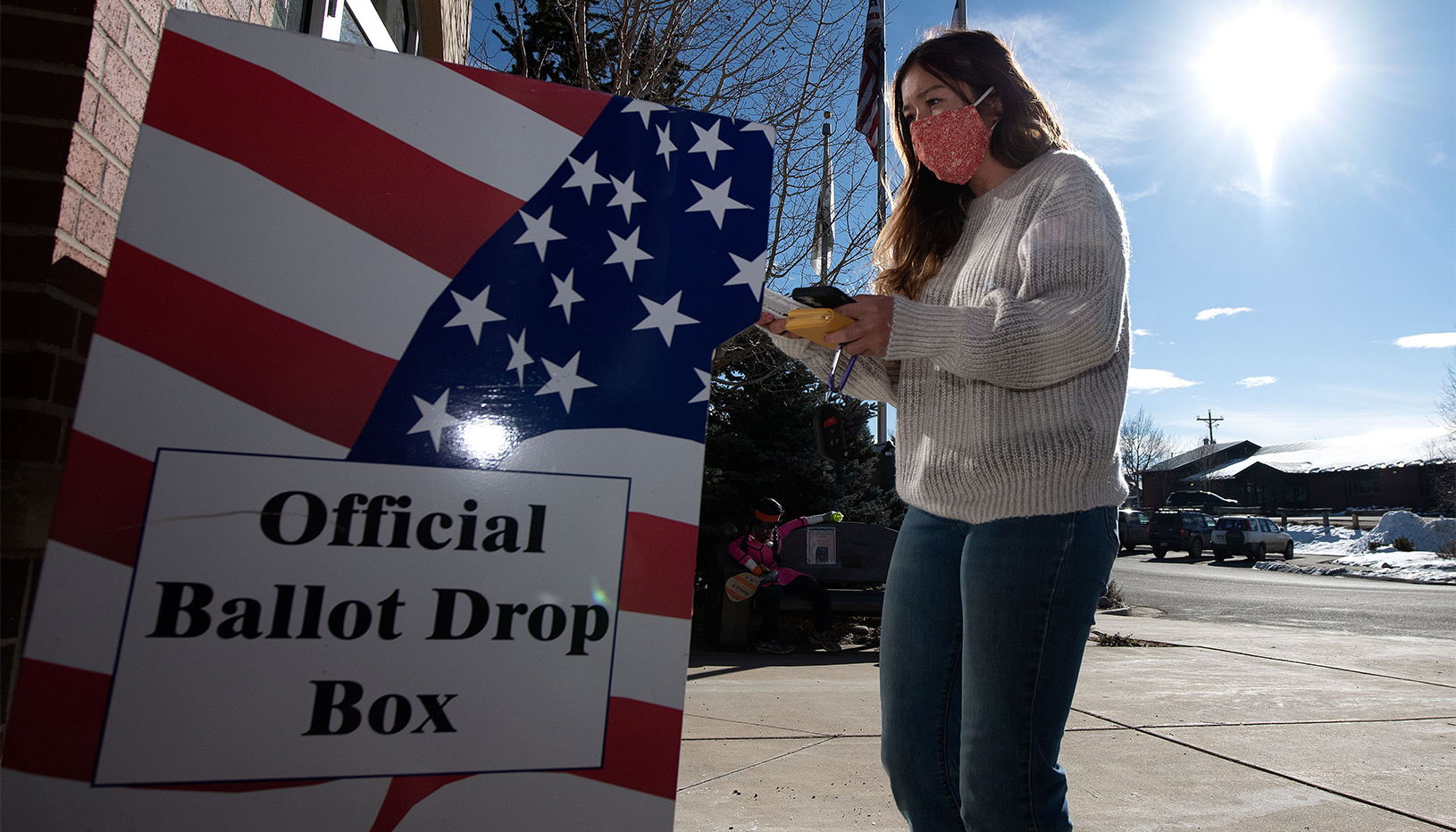 A person standing in front of a ballot drop box.