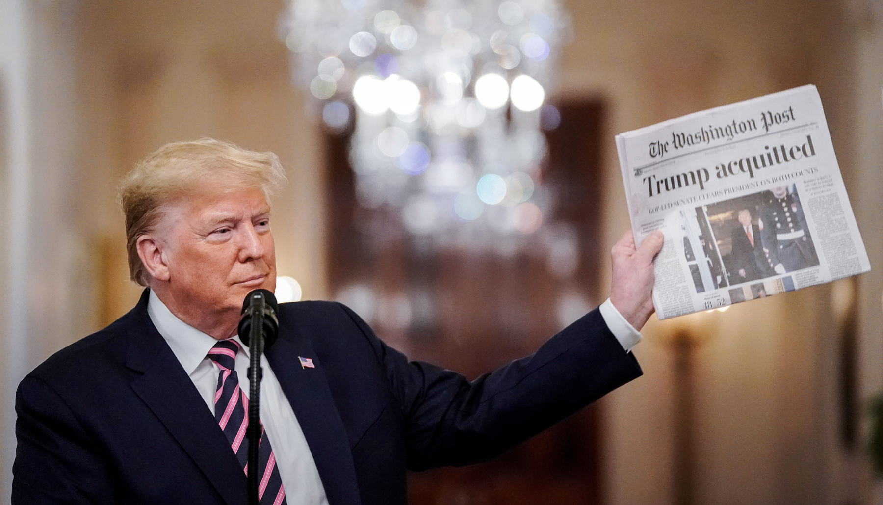 Former President Trump holds up a copy of the Washington Post that reads "Trump acquitted"