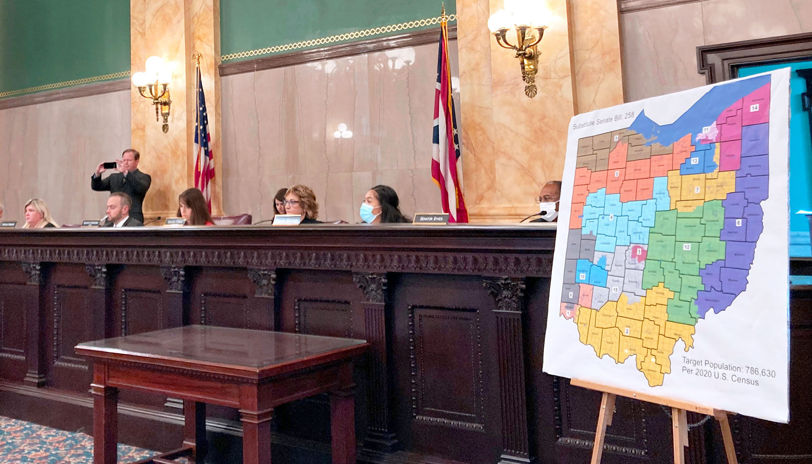 A panel of politicians sits by a large print of a proposed Ohio redistricting map on an easel