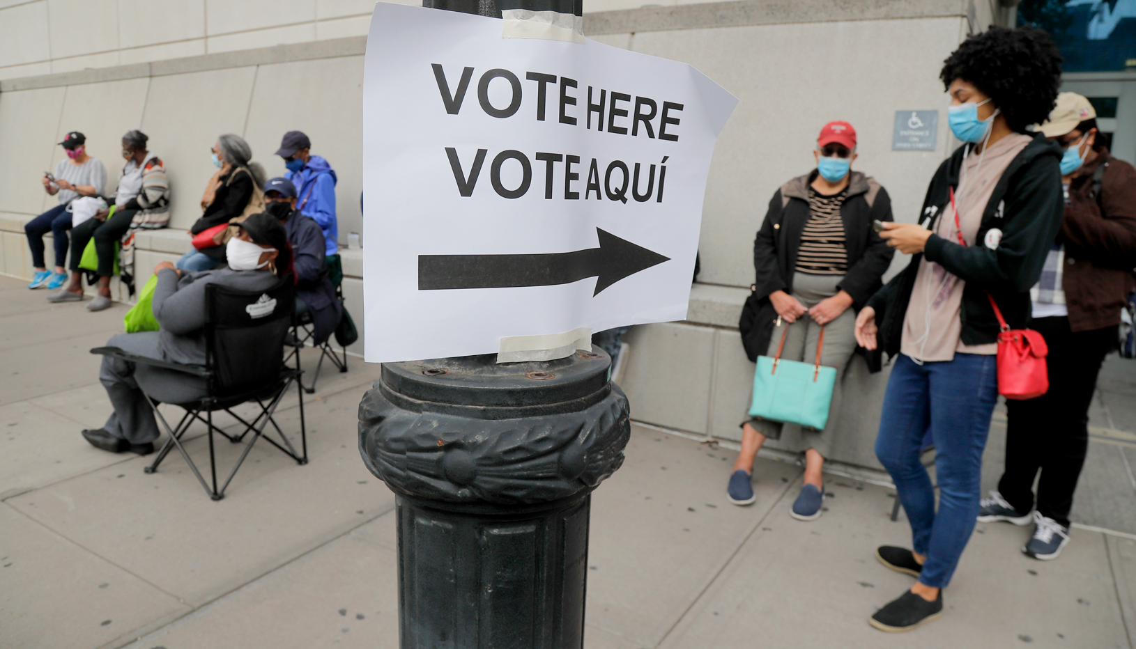 A bilingual English-Spanish "vote here" sign surrounded by voters in line