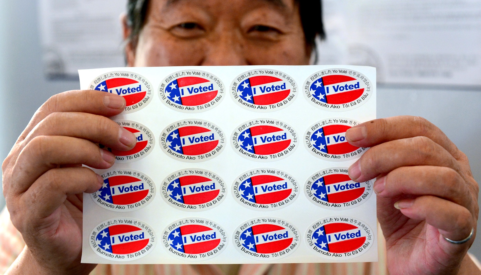 Asian American man holding "I Voted" stickers