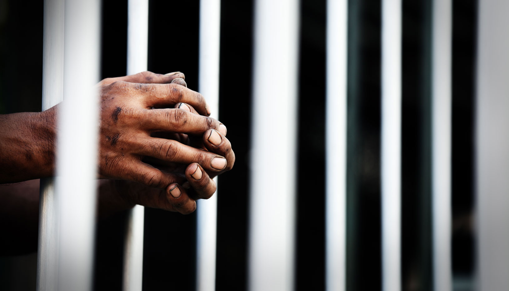 Prisoner's clasped hands resting on jail bars