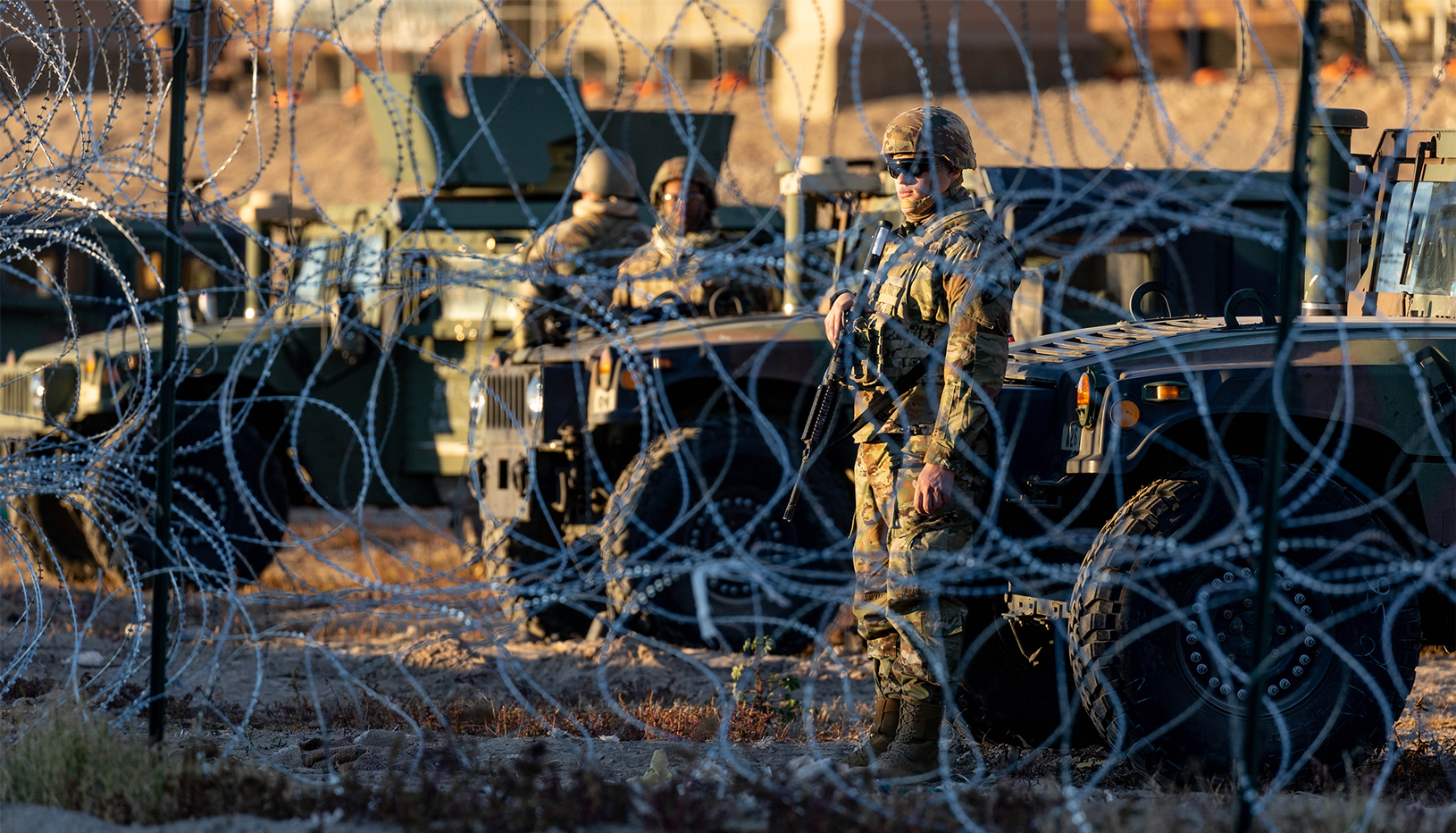 Texas National Guard troops at the border with barbed wire barrier in the background