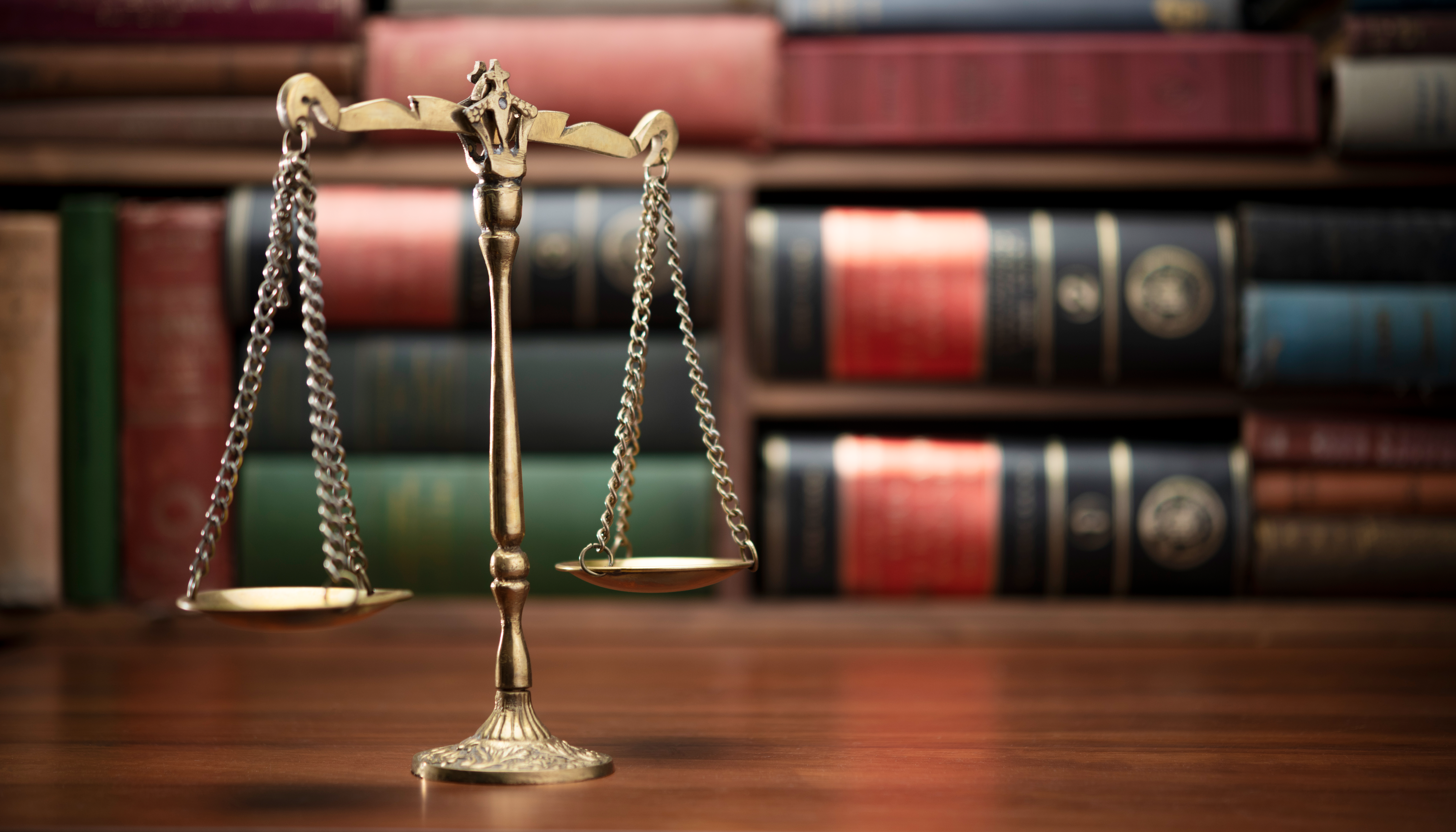 The scales of justice sit in front of legal books. 