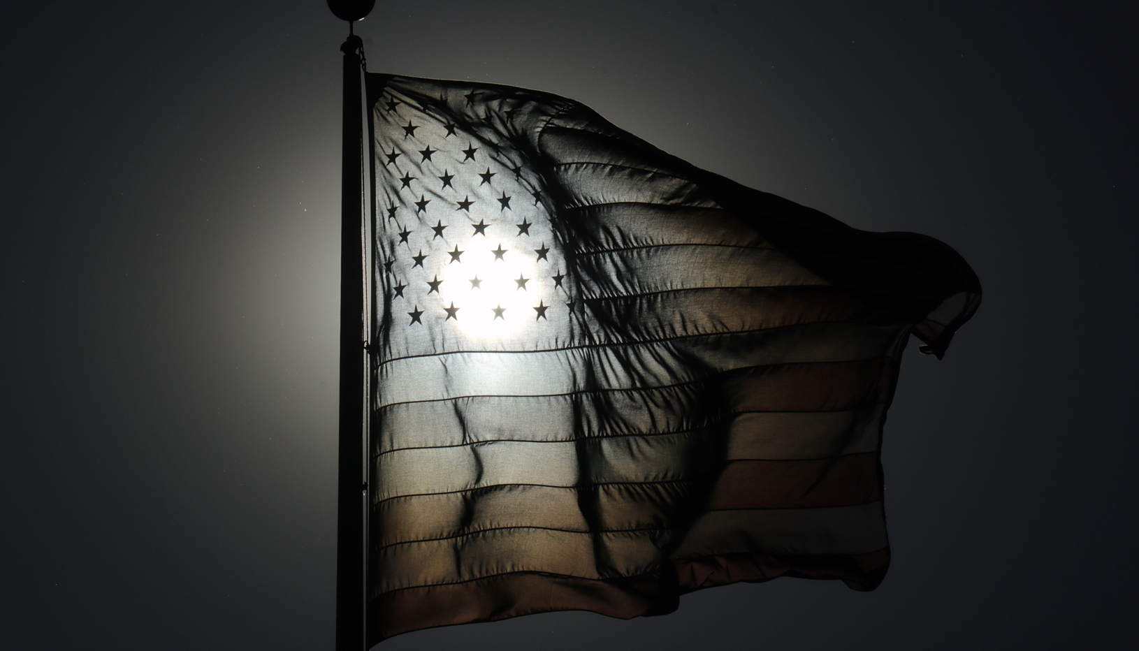 Black and white American flag image with sun shining through stars