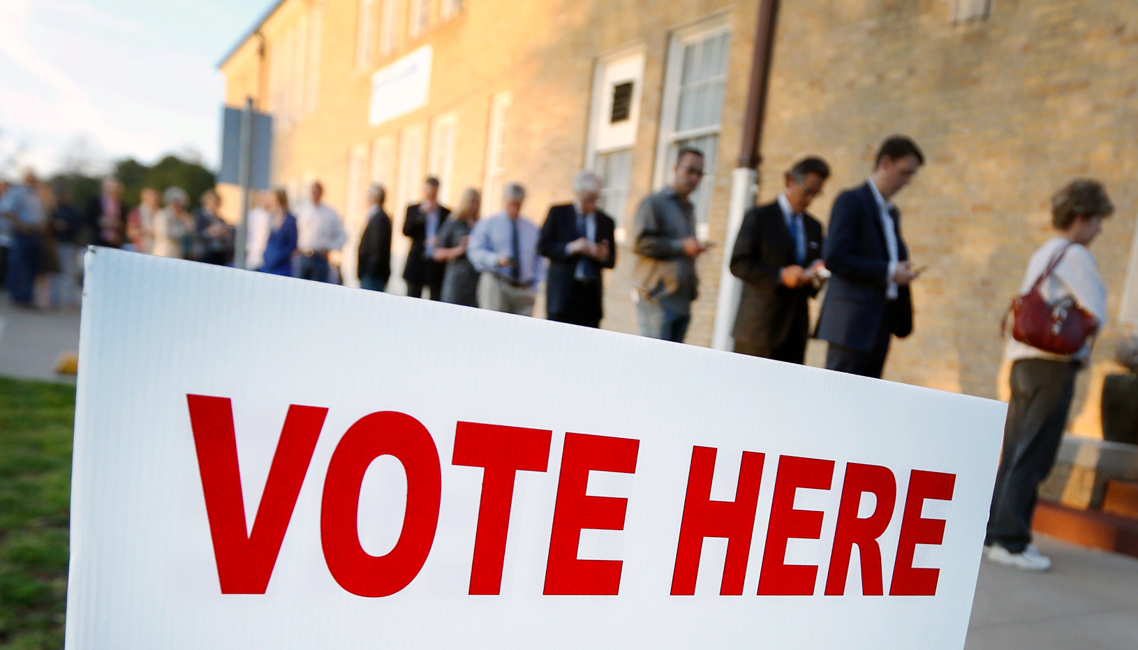 People in line to vote in background with Vote Here sign in foreground