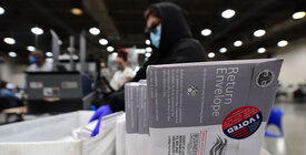 An election worker sorts mailed ballots, with a close up shot of one sealed with an "I Voted" sticker