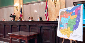 A panel of politicians sits by a large print of a proposed Ohio redistricting map on an easel