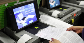 An election worker feeds a ballot into a scanner