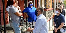 A Census-taker interviews a woman standing on her porch and carrying a baby