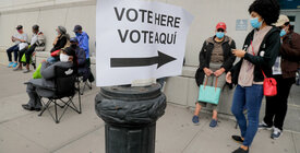 A bilingual English-Spanish "vote here" sign surrounded by voters in line