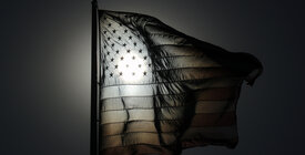 Black and white American flag image with sun shining through stars