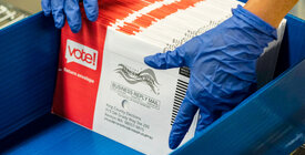 Gloved hands handling mail ballots