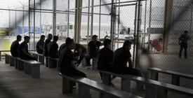 Men detained within a chain link fence