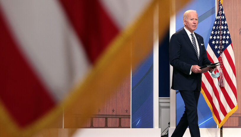 President Biden walks away from a podium, framed by American flags