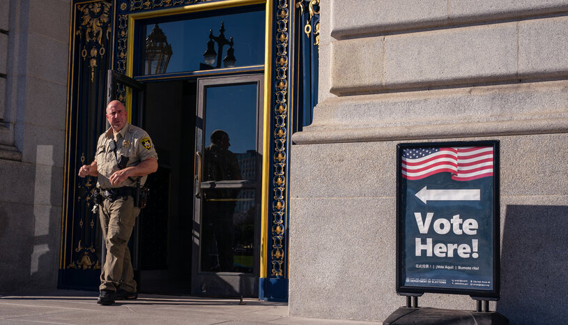 law enforcement officer outside polling place, near vote here sign