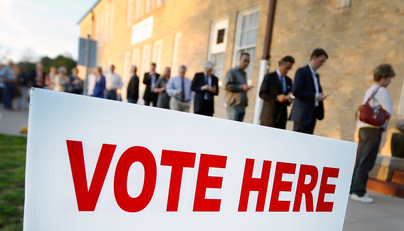 People in line to vote in background with Vote Here sign in foreground