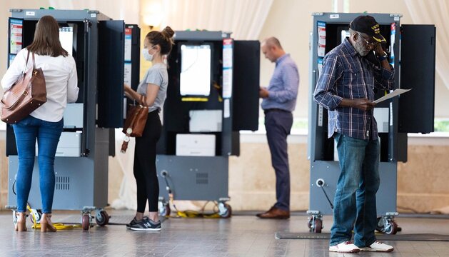 Four people standing near voting machines, either about to or currently submitting their votes