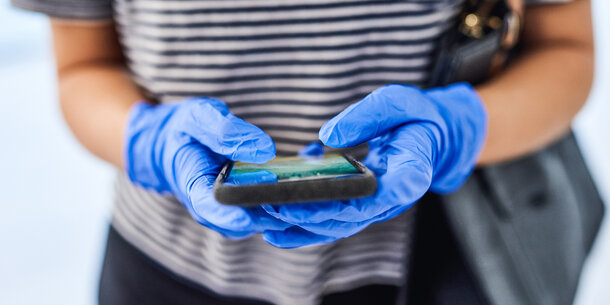 person wearing surgical gloves holding a smart phone
