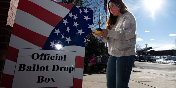 A person standing in front of a ballot drop box.