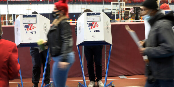 person walking past two voting booths while wearing a mask.