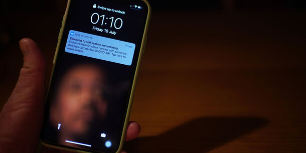 A man's face is reflected in a smartphone screen which shows a Covid-19 exposure notification