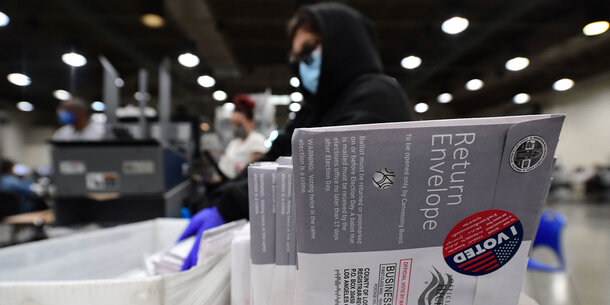 An election worker sorts mailed ballots, with a close up shot of one sealed with an "I Voted" sticker