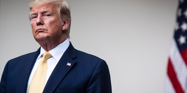 Former President Trump looks at the camera, with an American flag in the background