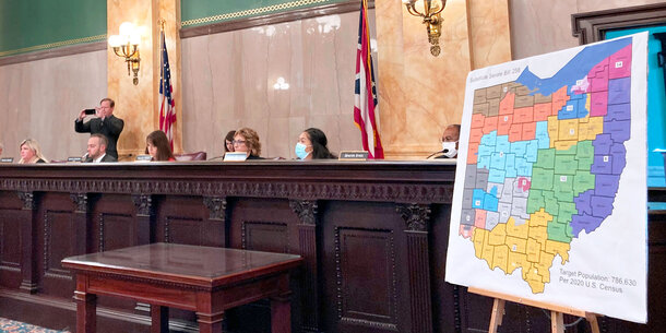 A panel of politicians sits by a large print of a proposed Ohio redistricting map on an easel