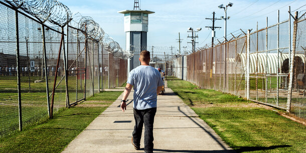 A man walks out of prison on a path between two barbed wire fences
