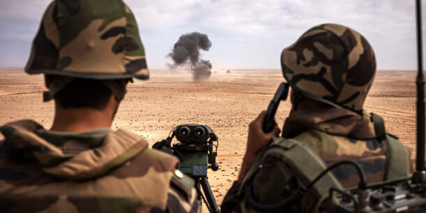 Two soldiers watch a distant explosion in the desert