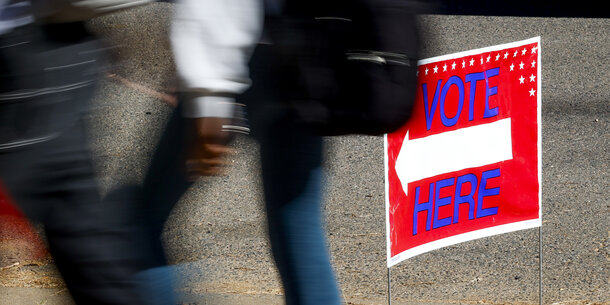 People walking past a vote here sign with an arrow