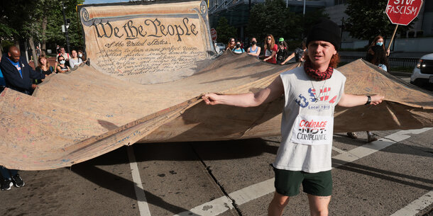 Photo of man carrying giant copy of the U.S. Constitution in demonstration. 
