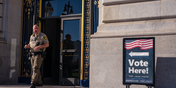 law enforcement officer outside polling place, near vote here sign