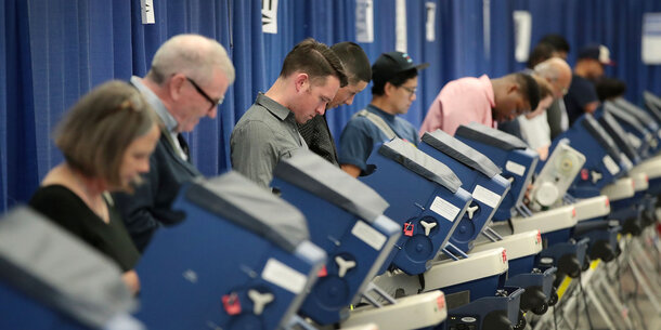 Line of voters at booths in front of blue curtain