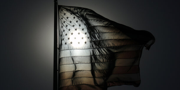 Black and white American flag image with sun shining through stars