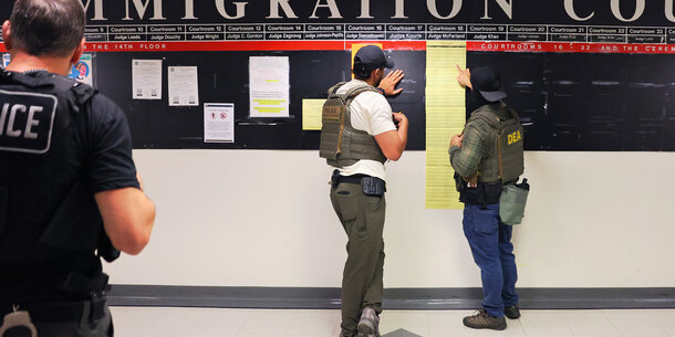 Three immigration enforcement agents in front of a sign that reads "Immigration Court"