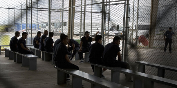 Men detained within a chain link fence