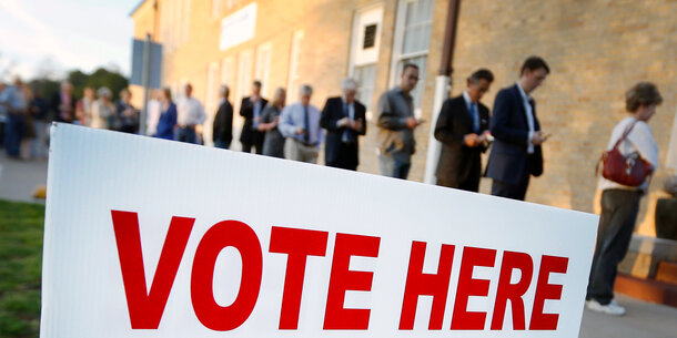People in line to vote in background with Vote Here sign in foreground