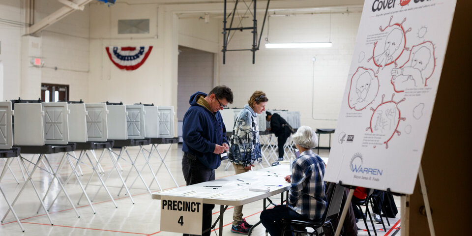 A poster with guidelines for safely coughing in the foreground of an image of a polling place.