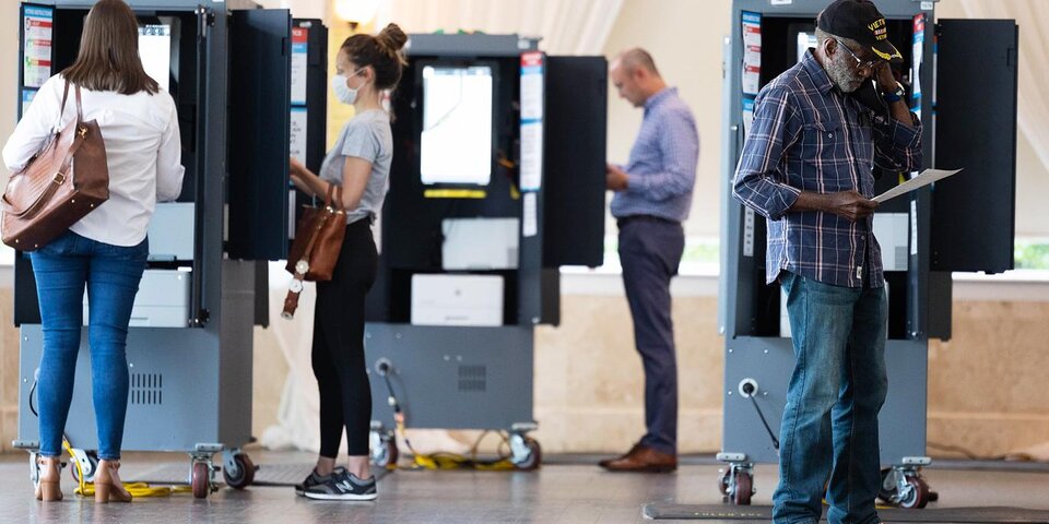 Four people standing near voting machines, either about to or currently submitting their votes