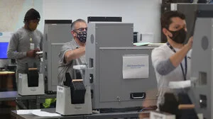 Three people in masks using voting machines to vote.
