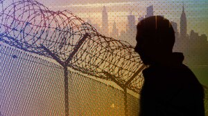 Man behind prison fence with New York City skyline behind him