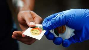 Poll worker wearing a glove is handing a voter a Georgia sticker.