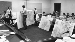 Black-and-white picture of map drawers moving and discussing large annotated maps