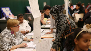 A hijabi woman speaks with an election worker from across a table