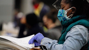 A masked election worker rifles through a stack of paper ballots