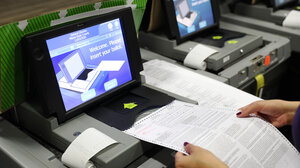 An election worker feeds a ballot into a scanner
