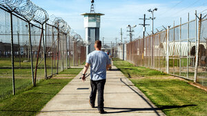 A man walks out of prison on a path between two barbed wire fences